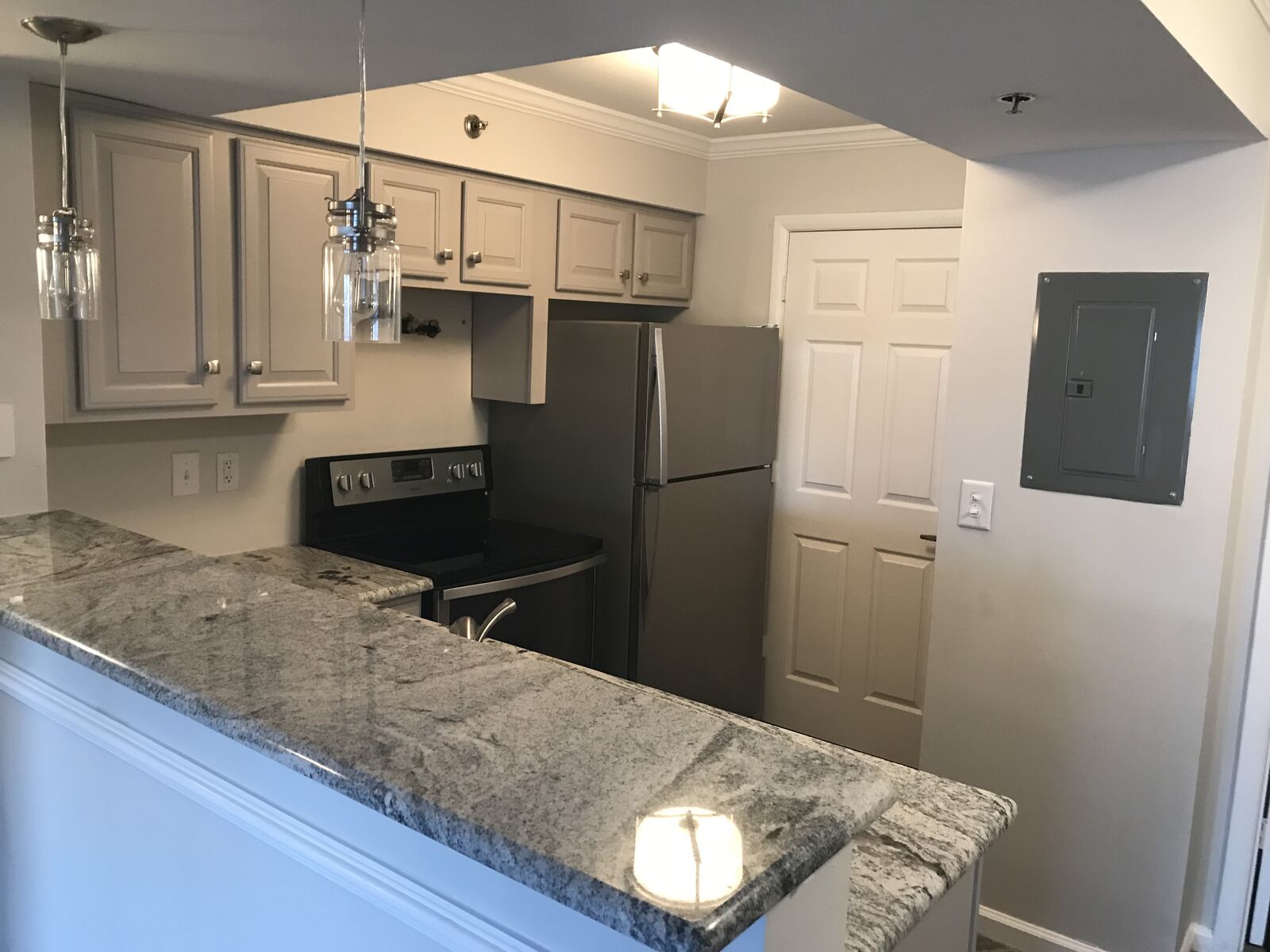 Apartment kitchen with gray cabinets, granite countertop and stainless steel refrigerator
