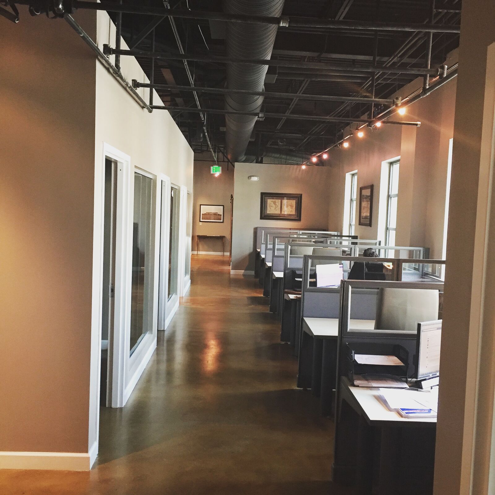 Commercial office corridor with glass offices, workstations and stained concrete floor